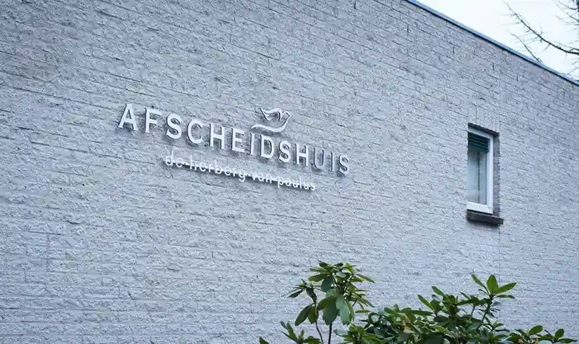 Vooraanzicht van een gebouw met grijze bakstenen met daarop 'Afscheidshuis'